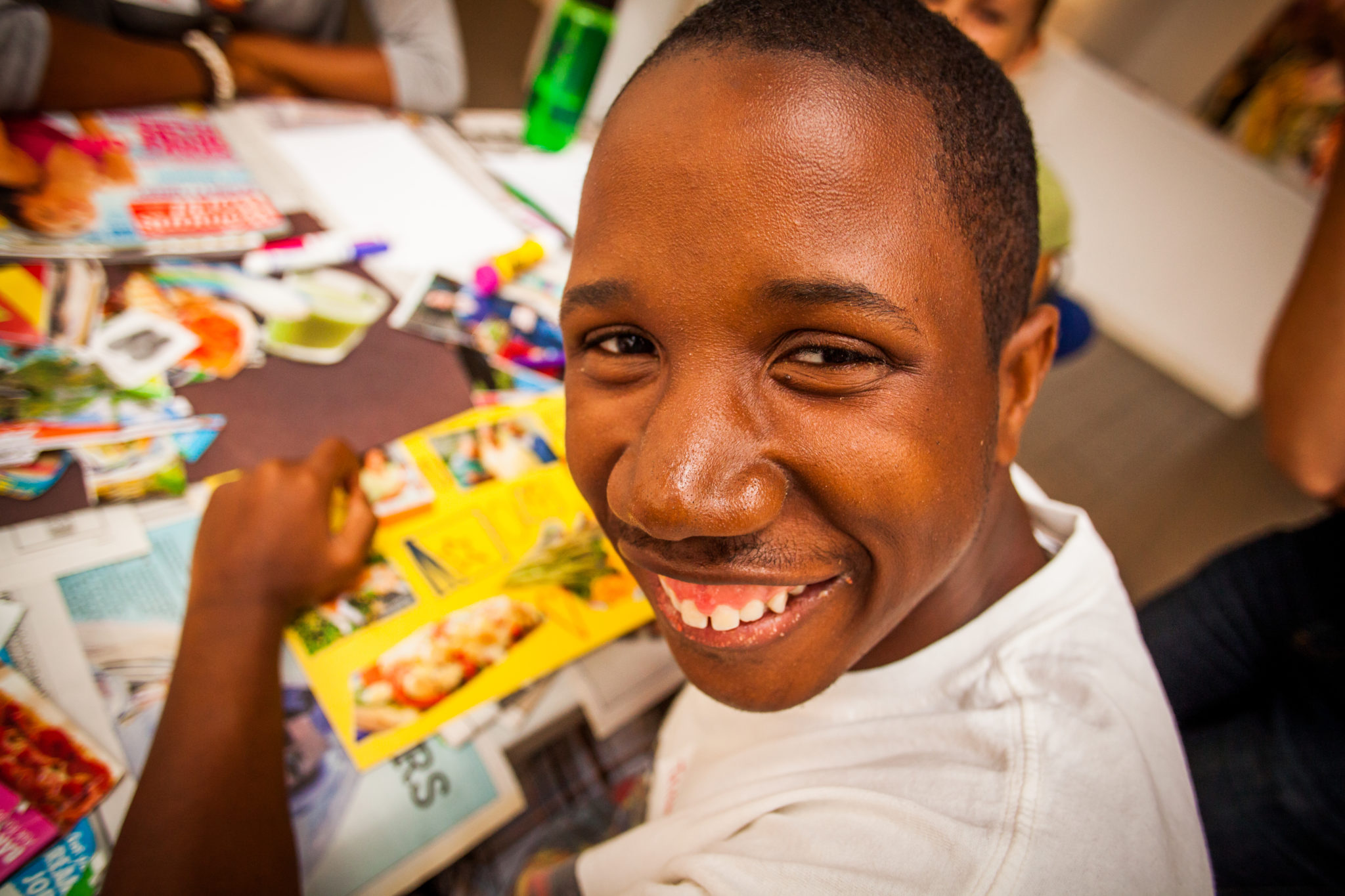 A young man smiles at the camera as he works on a collage.