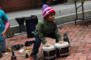 A small child beats excitedly on a pair of drums during Tony Mascara's presentation at Art-Reach's 30th birthday party.
