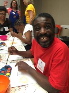 A SpArc program participant smiles for the camera while holding a brush dipped in watercolors, at a Barnes Foundation ArtSee event.