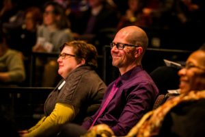 A male audience member smiles with his eyes closed .