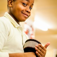 A boy raises his eyebrows and smiles while holding an instrument.