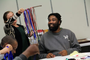 A man looks at a fiber art wall hanging as it is held up by an instructor at an Encore event.