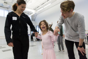 Two PA Ballet dancers hold hands with a young girl in a pink leotard and skirt at one of Art-Reach's Encore events.