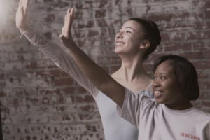 PA Ballet dancer and Saint Katherine Day School student extend their arms, palms flexed and open, while looking up and smiling.