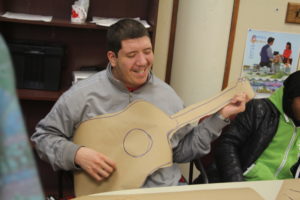 A man smiles while holding a paper guitar.