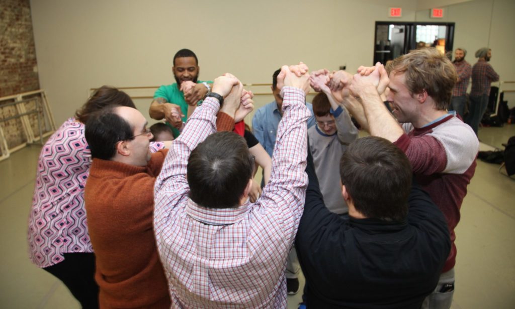 A group of PA Ballet dancers and students from Saint Katherine Day School hold hands and raise their arms in a circle.