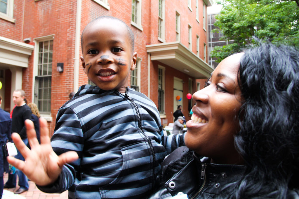 Three year old boy with face paint held by his mother smiling