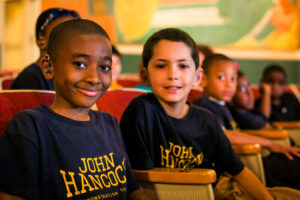 Two boys with hearing aids smile at the camera.