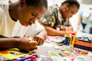 A boy creates a collage, with colourful paper clippings spread out on the table in front of him.