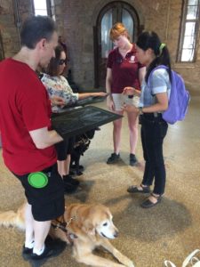 Guests of Eastern State Penitentiary's guided tour stop and feel raised map with Angela Standing by. Their service dogs sit at their feet.