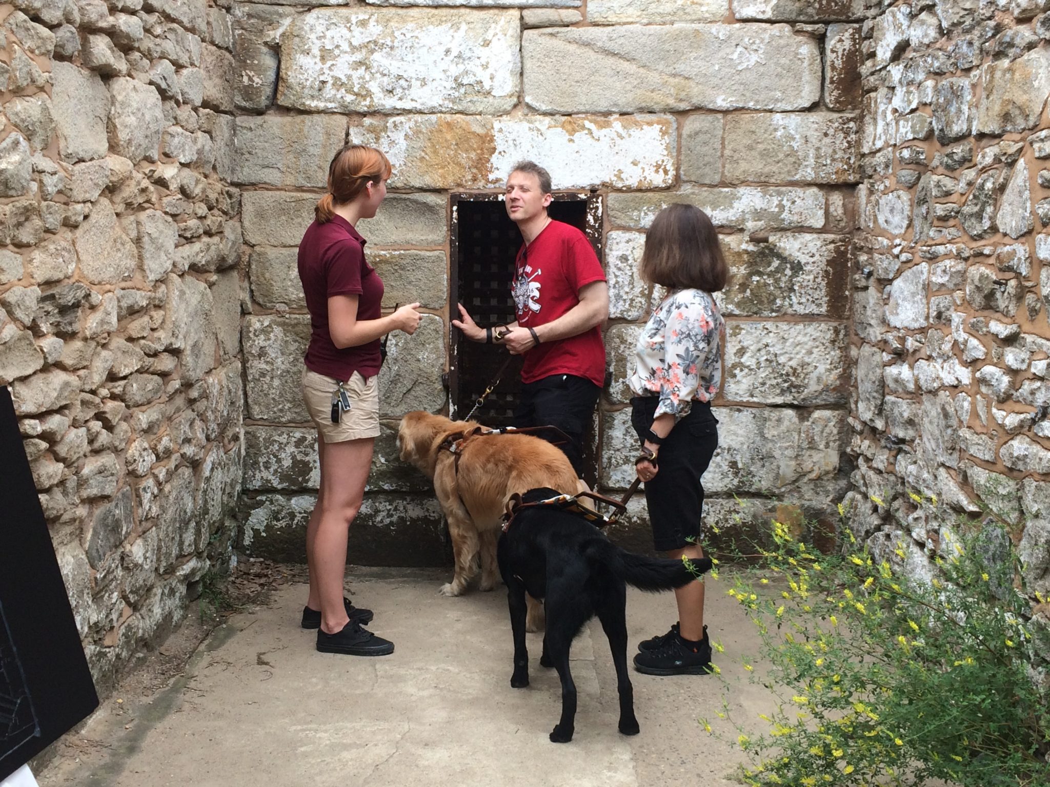 Tour Guide explains the impotance of small doorway in jail cell. Guests feel the threshold of the door while holding the leash of his service dog