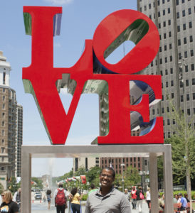 Lewis Johnson standing in front of the LOVE Statue with the packdrop of teh crowded parkway behind him