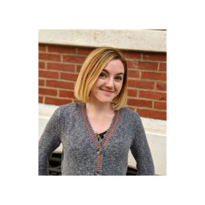 Photo of Alex boyle in sweater smiling against brick wall