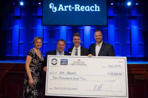 John, Comcast and Ovation team members posing with john behind a 5 foot check made out to Art-Reach from Ovation