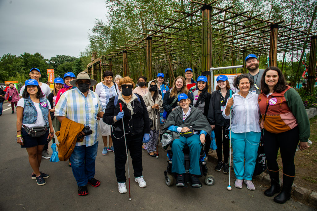 A large outdoor group shot of Art-Reach staff members and people who are blind or low vision. Everyone is facing the camera and smiling.