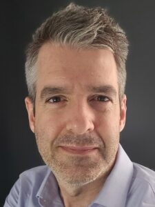 White man with salt and pepper hair in front of a dark background.