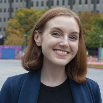 Alex Boyle, a white woman with shoulder length red hair, wearing navy blazer and black shirt