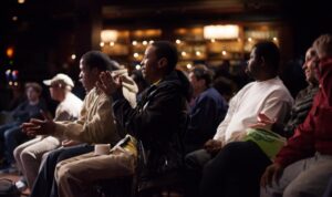 a small, diverse crowd of people sitting in a concert hall, clapping