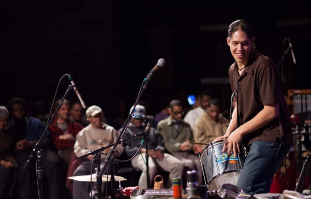 a person with ligh skin tone and ong black hair playing the drums at an art-reach encore event