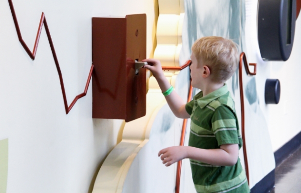 child with light skin interacting with a switch in museum exhibit