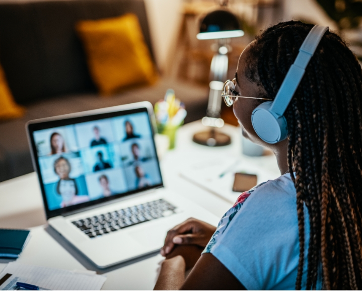 black woman with dark skin and braids watching a conference call on a laptop in a living room